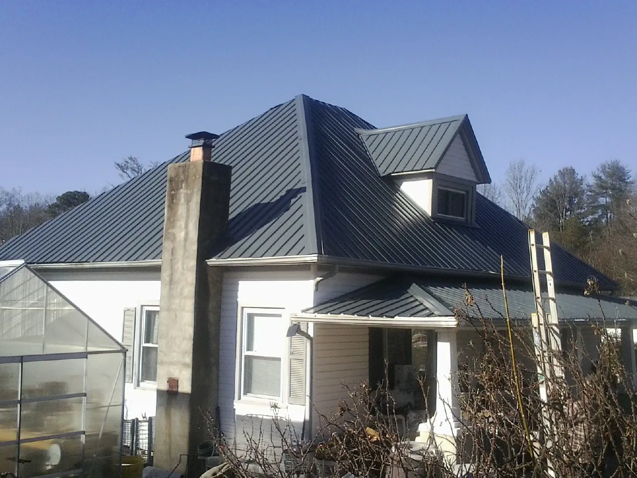 Dark blue standing seam metal roof on a white farmhouse with dormer — Slate & Tile Roof Repair by Roofing Brothers in Manitou Springs