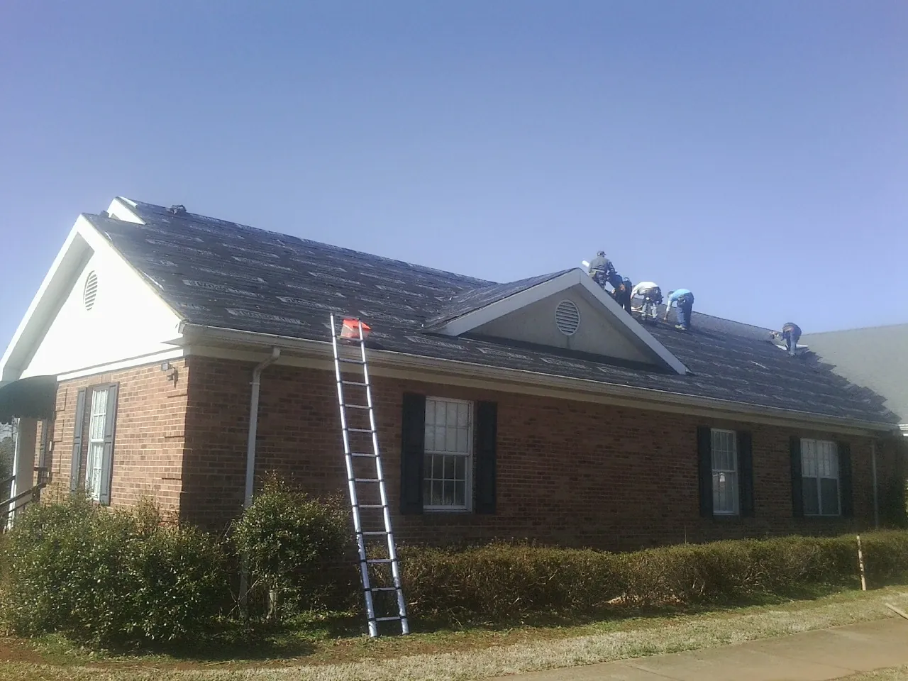 Crew tearing shingles off a brick ranch roof with a ladder set — Emergency Roof Repair work by our crew in Manitou Springs