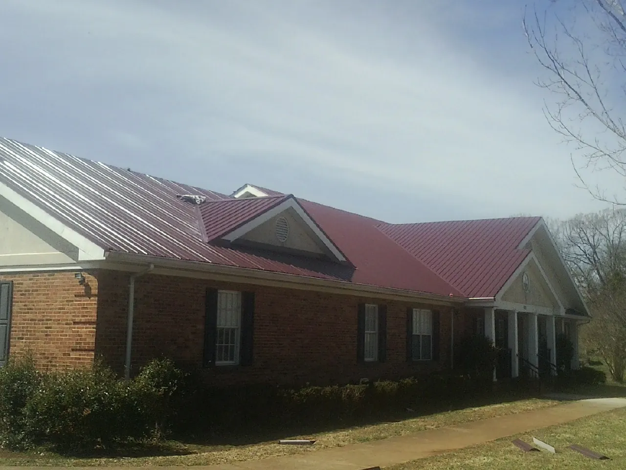 Red metal roof with gabled entries on a long brick building, from a Hail Damage Roof Repair job in Manitou Springs