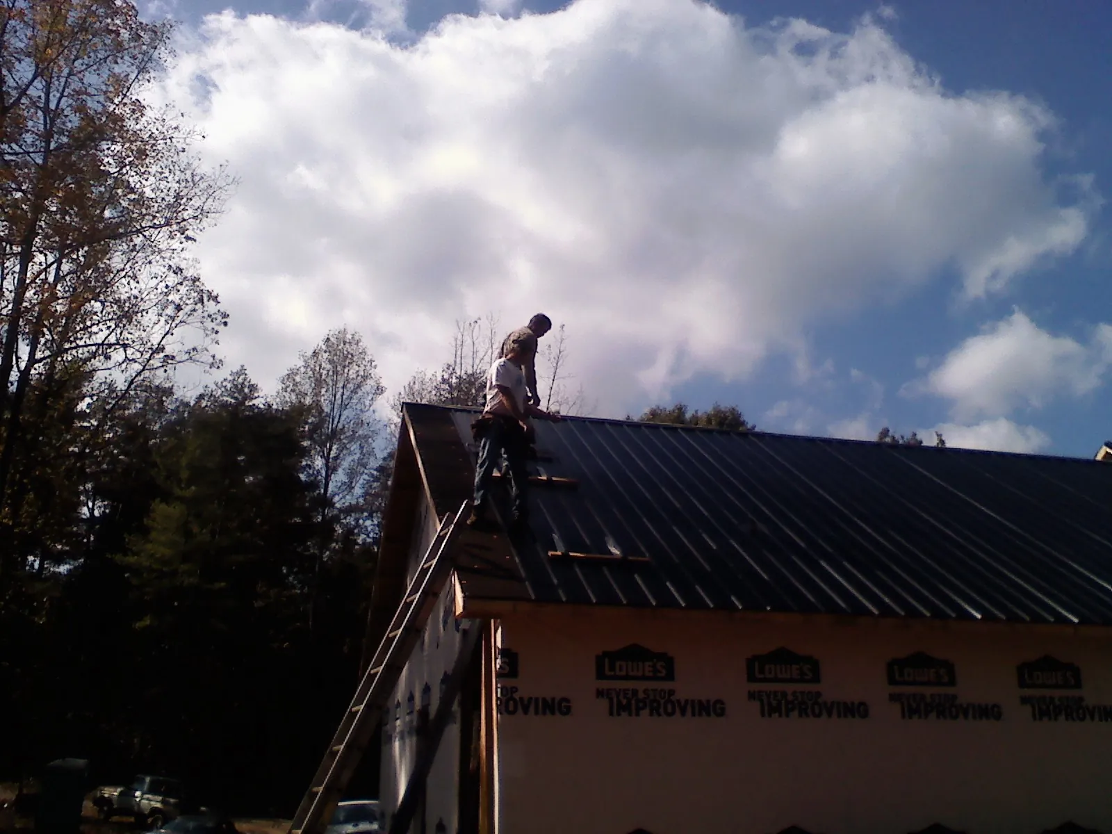 Roofer fastening dark metal panels high against a cloudy sky, from a Roof Inspection job in Manitou Springs