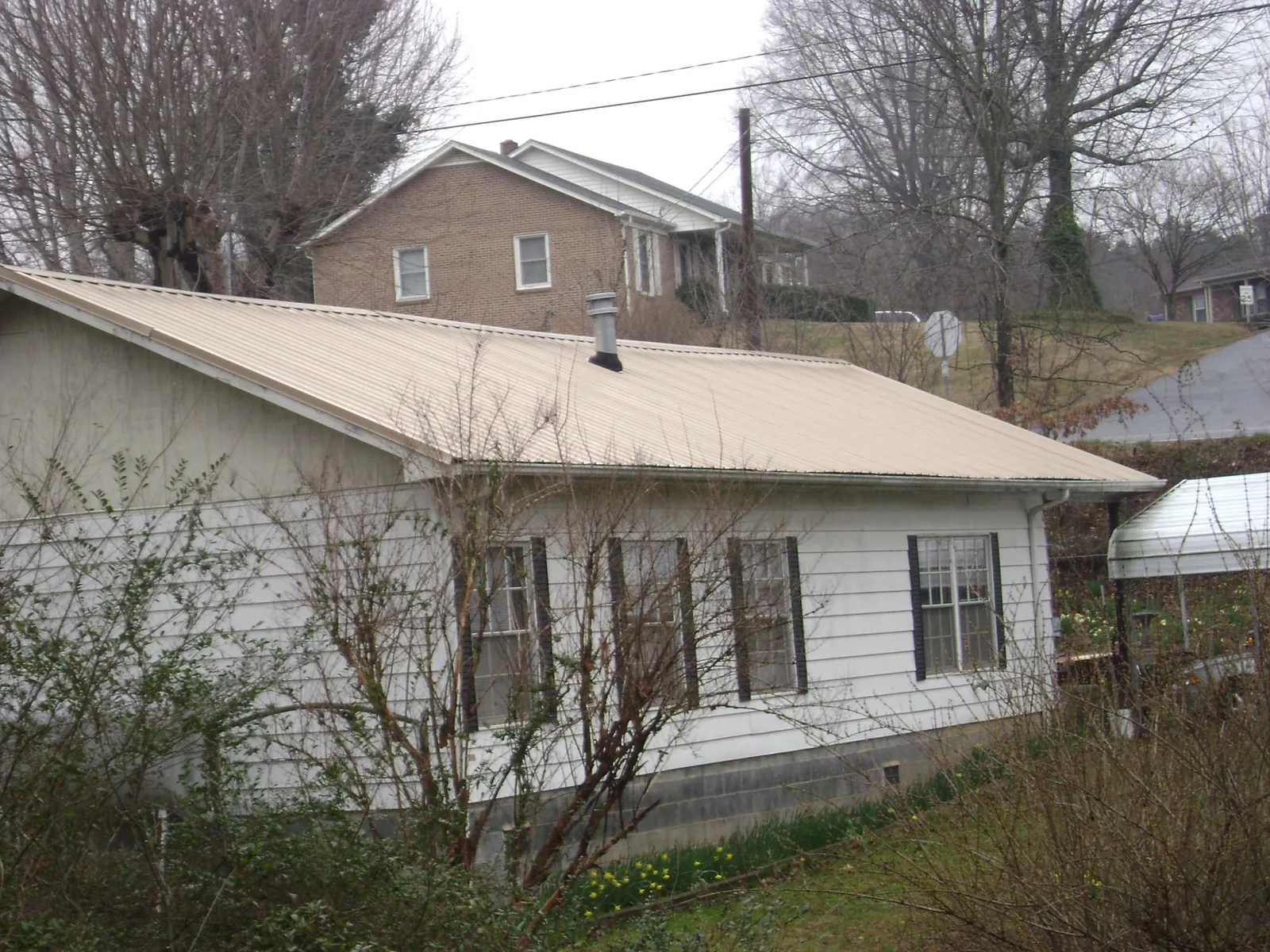 Tan metal roof on a white sided house set into a hillside — Commercial Roofing by Roofing Brothers in Manitou Springs