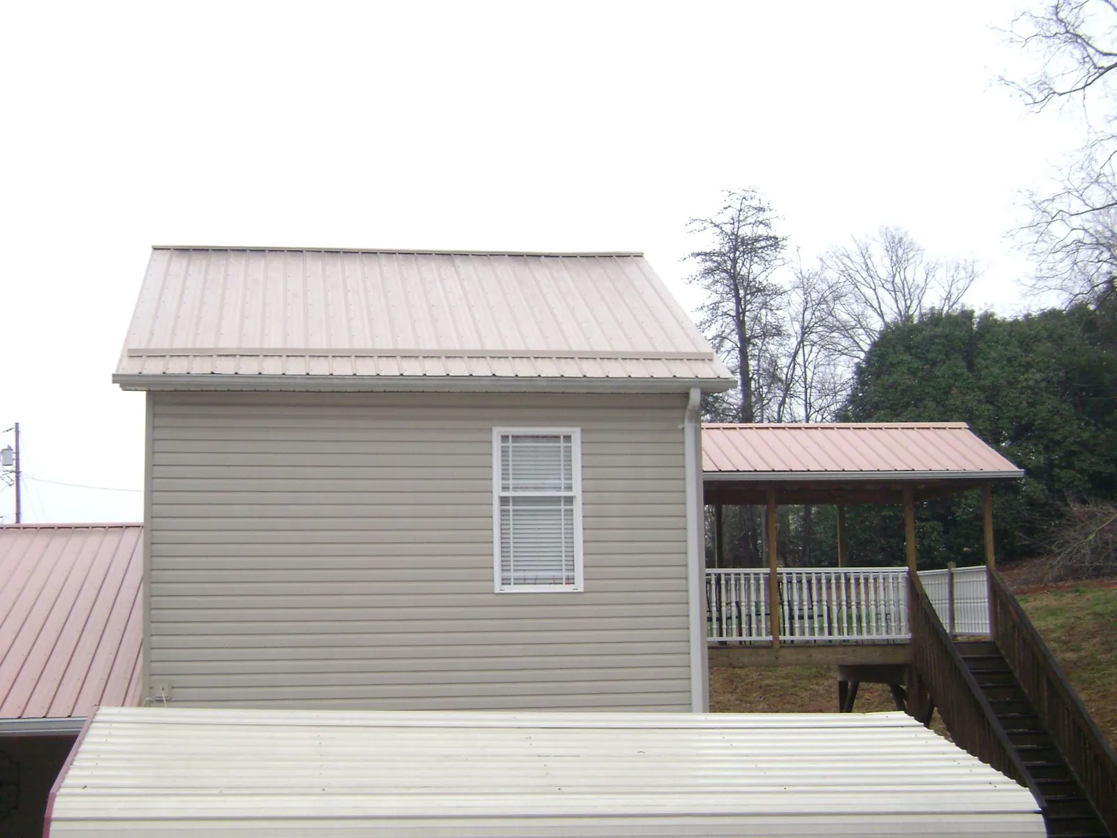 Tan metal roofs on a two story addition and attached porch, from a Roof Replacement job in Manitou Springs